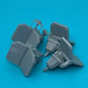 May include: Four gray plastic model airplane parts, possibly landing gear, on a blue background.