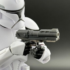May include: A white action figure of a Star Wars clone trooper holding a black blaster pistol. The figure is wearing a white helmet with black markings.