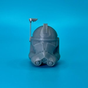 May include: A gray plastic Star Wars clone trooper helmet with a black visor and a small antenna on top.