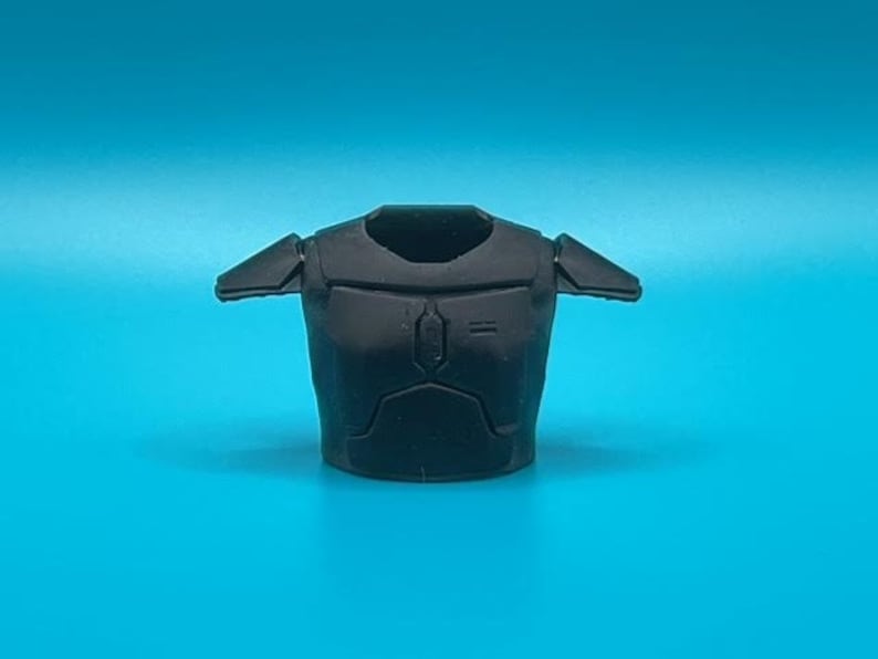 May include: Black plastic armor piece for a toy action figure. The armor has a textured surface and is designed to resemble a futuristic warrior's chest plate.
