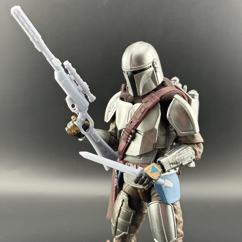 Puede incluir: Figura de acci&oacute;n detallada de un personaje de una serie de ciencia ficci&oacute;n. La figura est&aacute; vestida con una armadura plateada con un casco y una correa marr&oacute;n para el hombro. Sostiene un rifle blanco y una espada blanca. La figura tiene un guantelete de mu&ntilde;eca azul y dorado.