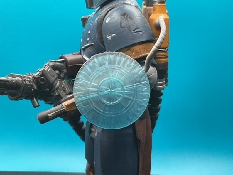 May include: A blue and gray action figure with a translucent blue shield, a brown belt, and a gray and black blaster.