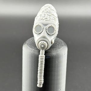 May include: A grey gas mask with a textured surface and two round eye pieces. The mask has a long, ribbed hose attached to the bottom.
