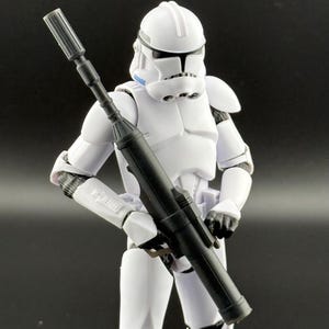 May include: A white action figure of a Star Wars clone trooper holding a black blaster rifle. The figure has a white helmet with a blue visor.