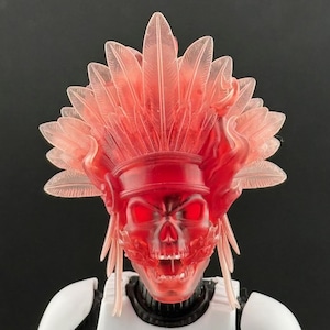 May include: A red translucent skull-shaped mask with glowing red eyes and a feathered headdress. The mask is part of a white and black costume, likely a cosplay or collectible item. The headdress features feather-like details.