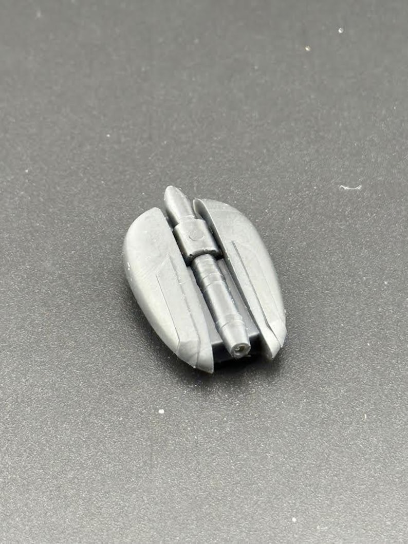 May include: A grey plastic model of a futuristic weapon, resembling a futuristic gun or cannon, with a cylindrical barrel and a rounded, slightly curved body.