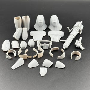 Peut inclure: Ensemble de pi&egrave;ces d&eacute;tach&eacute;es de maquette en plastique gris clair, non assembl&eacute;es. Les composants comprennent des sections de casque, des pi&egrave;ces de torse, des armures de bras et de jambes, une ceinture et une grosse arme avec un petit pistolet.