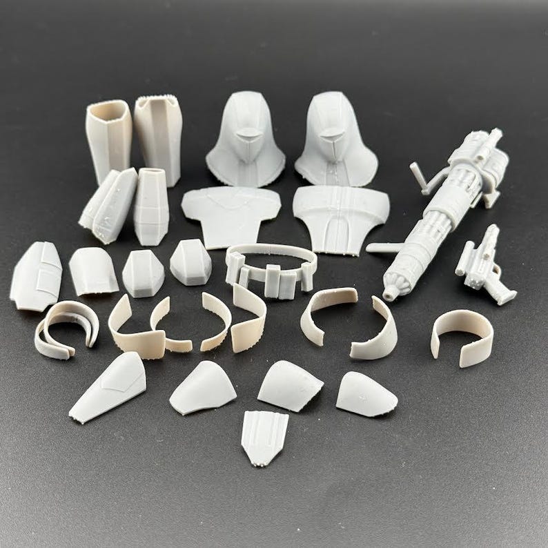 Peut inclure: Ensemble de pi&egrave;ces d&eacute;tach&eacute;es de maquette en plastique gris clair, non assembl&eacute;es. Les composants comprennent des sections de casque, des pi&egrave;ces de torse, des armures de bras et de jambes, une ceinture et une grosse arme avec un petit pistolet.
