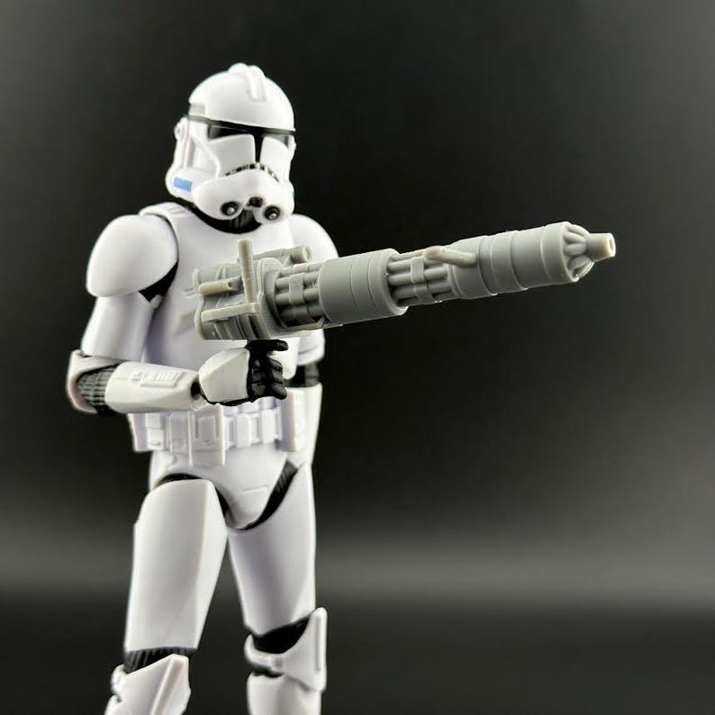 Peut inclure: Figurine blanche d'un Stormtrooper de Star Wars, tenant un blaster gris. La figurine est en position debout, avec un casque et une armure d&eacute;taill&eacute;s. Le blaster est une arme cylindrique &agrave; plusieurs canons.