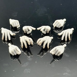 May include: A collection of small, light-colored, articulated hands. The hands are in various poses, including open palms, fists, and pointing gestures. The hands are likely intended for use with action figures or similar models.