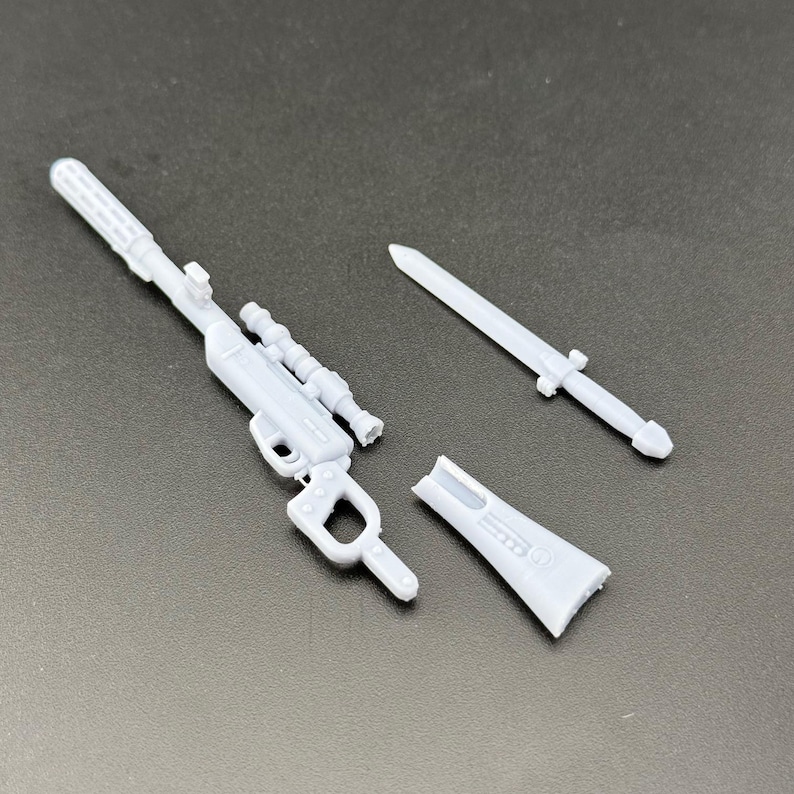 Puede incluir: Un juego de armas de juguete de pl&aacute;stico gris claro, que incluye un rifle con mira telesc&oacute;pica, una espada y una pieza separada. El rifle tiene un dise&ntilde;o detallado con ca&ntilde;&oacute;n y empu&ntilde;adura. La espada es una hoja simple y puntiaguda. La pieza separada parece ser parte del rifle.