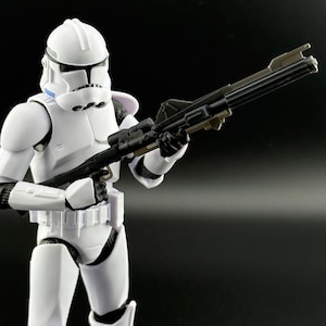 Peut inclure: Une figurine blanche d'un clone trooper de Star Wars tenant un fusil blaster noir. La figurine porte un casque blanc avec une visière bleue.