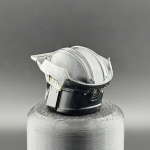 Pu&ograve; includere: Un casco in plastica nera con una superficie testurizzata e un design in rilievo sulla parte superiore. Il casco ha una visiera e un cinturino per il mento.