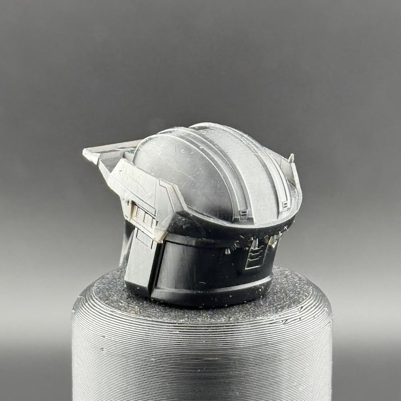 Pu&ograve; includere: Un casco in plastica nera con una superficie testurizzata e un design in rilievo sulla parte superiore. Il casco ha una visiera e un cinturino per il mento.
