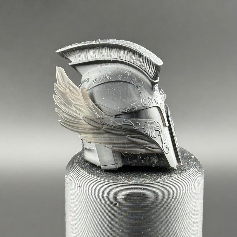 May include: A black and silver helmet with a winged design. The helmet has intricate details and a textured surface.