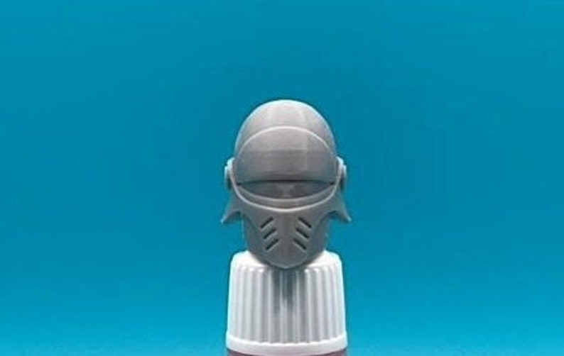 May include: A grey plastic helmet with a visor and a face mask. The helmet has a textured surface and a design on the front.