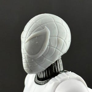 May include: Close-up of a gray Spider-Man action figure head. The mask features a webbed design and large eye openings. The figure's neck is black, and the body is white. The figure is a collectible toy.