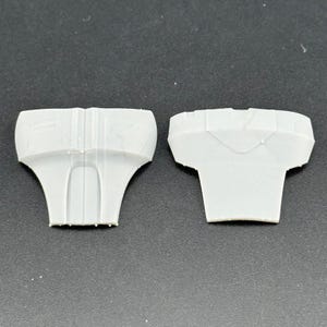 Peut inclure: Deux composants en plastique gris clair, possiblement des pi&egrave;ces d'un assemblage plus grand, sont pr&eacute;sent&eacute;s sur un fond neutre. Chaque pi&egrave;ce a une forme unique, avec un dessus large et une base &eacute;vas&eacute;e plus &eacute;troite.