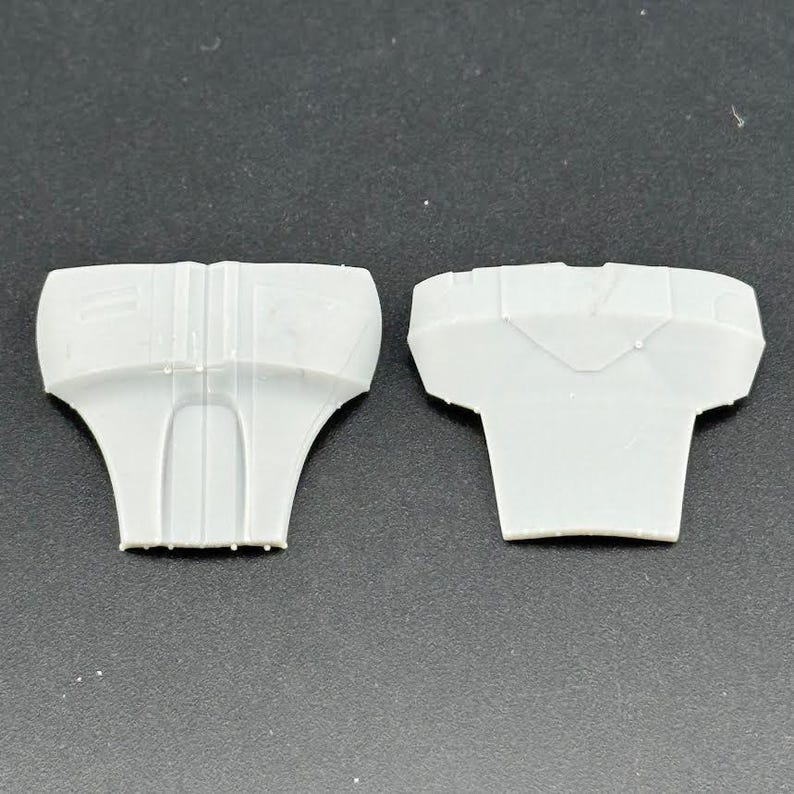 Peut inclure: Deux composants en plastique gris clair, possiblement des pi&egrave;ces d'un assemblage plus grand, sont pr&eacute;sent&eacute;s sur un fond neutre. Chaque pi&egrave;ce a une forme unique, avec un dessus large et une base &eacute;vas&eacute;e plus &eacute;troite.