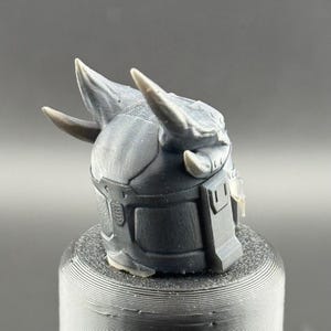 May include: A 3D printed helmet with two horns, a textured surface, and a dark gray color.