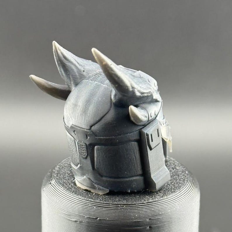 May include: A 3D printed helmet with two horns, a textured surface, and a dark gray color.