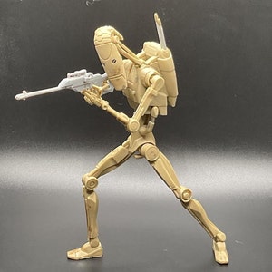 May include: A beige plastic action figure of a Star Wars battle droid holding a blaster rifle. The droid has a detailed design with articulated limbs and a backpack.