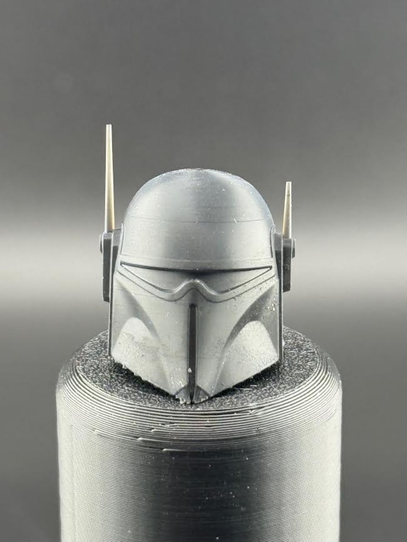 May include: A black plastic helmet with two small antennas on top. The helmet has a visor and a textured surface.