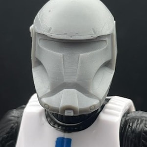 Puede incluir: Un casco de pl&aacute;stico blanco con una m&aacute;scara facial gris. El casco tiene una superficie texturizada y un dise&ntilde;o en relieve en la parte superior. La m&aacute;scara facial tiene una visera y una serie de l&iacute;neas y ranuras.