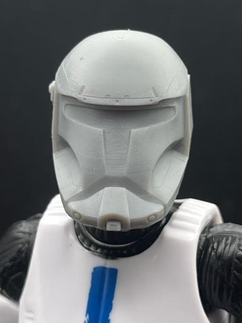 Puede incluir: Un casco de pl&aacute;stico blanco con una m&aacute;scara facial gris. El casco tiene una superficie texturizada y un dise&ntilde;o en relieve en la parte superior. La m&aacute;scara facial tiene una visera y una serie de l&iacute;neas y ranuras.