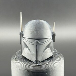 May include: A black helmet with a visor and two antennas. The helmet has a textured surface and a V-shaped design on the front.