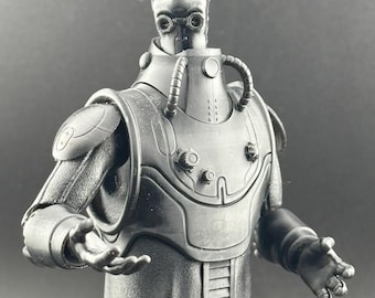 May include: A black and gray action figure of a robot with a detailed, textured, and articulated body. The robot has a large head with a black visor and a black and gray chest piece with a series of tubes and knobs.