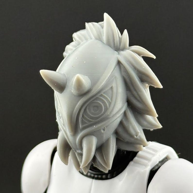 May include: A close-up of a gray, horned helmet with intricate eye-like designs and a spiky, textured crown. The helmet is part of a white Stormtrooper-style armor, suggesting a sci-fi or cosplay theme.