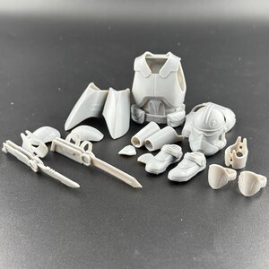 May include: A collection of unassembled, light grey miniature action figure parts. Includes a helmet, armour, boots, and various weapon components. The pieces are arranged on a dark surface.
