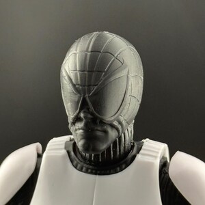 May include: A close-up of a black and white action figure's head and upper torso. The figure has a textured, web-like design on the helmet and large, stylized eye coverings. The figure is wearing a white chest piece.