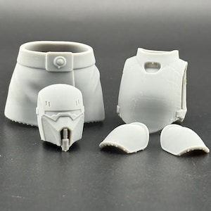 May include: A collection of unpainted, gray miniature armor pieces. Includes a helmet, chest piece, shoulder pads, and a belt-like piece. The pieces are likely for a model or figurine.