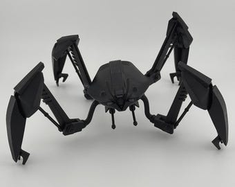 Könnte beinhalten: Ein schwarzes, artikuliertes, mehrbeiniges Roboter-Spielzeug mit einem detaillierten Kopf und segmentierten Gliedmaßen.