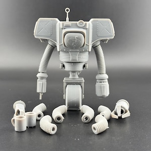 May include: A gray, assembled robot model with a central body, two articulated arms, and a single wheel. The robot has a detailed design with a circular emblem on its chest and several detached parts, including flexible tubes and small cups.