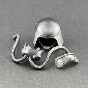 May include: A black plastic gas mask with a black helmet and a black and silver breathing tube. The gas mask has a clear visor and a black strap.