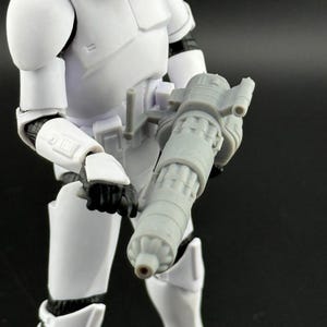 Peut inclure: Figurine d'un Stormtrooper de Star Wars blanc tenant une arme blaster grise. La figurine porte une armure blanche avec des d&eacute;tails noirs. Le blaster est cylindrique avec des &eacute;l&eacute;ments m&eacute;caniques d&eacute;taill&eacute;s.