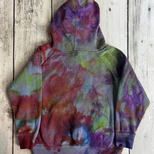 May include: A tie-dye hoodie in shades of purple, red, blue, and green. The hooded sweatshirt has a drawstring and ribbed cuffs and hem. The back of the hoodie is visible, showing the colorful, blended pattern.