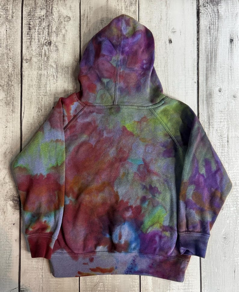 May include: A tie-dye hoodie in shades of purple, red, blue, and green. The hooded sweatshirt has a drawstring and ribbed cuffs and hem. The back of the hoodie is visible, showing the colorful, blended pattern.
