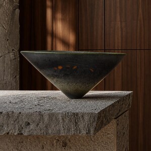 May include: A conical bowl with a dark, mottled charcoal and forest green exterior finish. The surface features a series of small, distinct orange circular accents arranged in a horizontal line near the upper rim of the vessel.