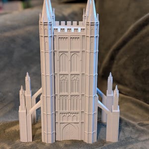 May include: A white architectural model of a cathedral with multiple spires and arched windows. The model has a detailed facade, including a central doorway and side towers. The structure is set against a soft, textured background.