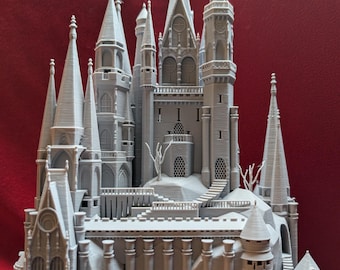 May include: A detailed 3D printed model of a gray castle with multiple towers and intricate details. The castle is set on a rocky base with a staircase leading up to the main entrance.