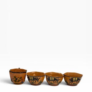 May include: A set of four tan ceramic bowls with a hexagonal rim. One bowl features a green cactus design, while the other three bowls are decorated with black and yellow illustrations of donkeys walking through green grass against a tan background.