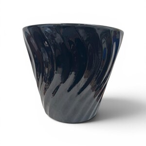 May include: A glossy, dark navy blue ceramic vase with a spiral design. The vase has a wide opening and a tapered base. The surface reflects light, highlighting the curved lines of the design. The vase is a decorative item.
