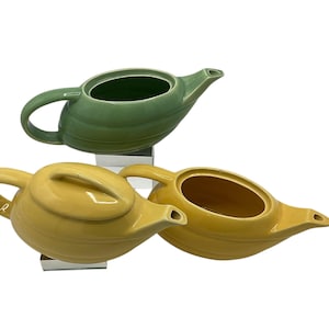 May include: Three ceramic teapots in different colors. A green teapot, a yellow teapot, and a yellow teapot with a lid.