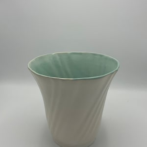 May include: A white ceramic vase with a light blue glaze on the inside. The vase has a twisted design and a wide opening.