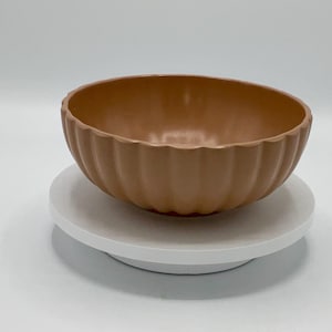 May include: A brown ceramic bowl with a fluted design sits on a white pedestal.
