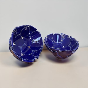 May include: Two deep, bowl-shaped objects constructed from numerous glossy, dark blue, circular ceramic pieces joined together. The structure of each bowl features open gaps between the individual blue discs, creating a textured, lattice-like appearance.